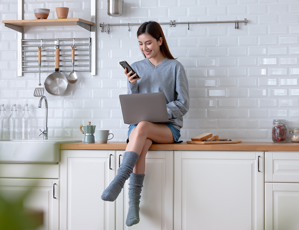 Smiling client sitting in a clean bright kitchen and checking her phone